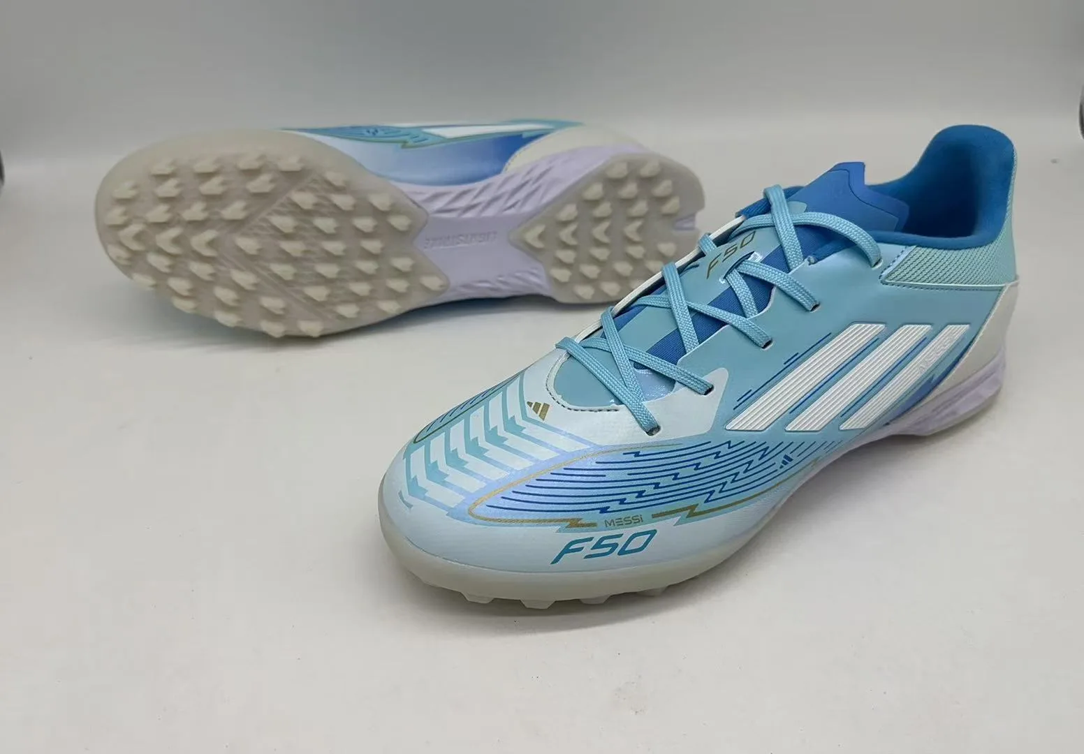 Adidas F50 Elite TF (em tom azul-claro, azul-escuro, branco e detalhes em dourado).